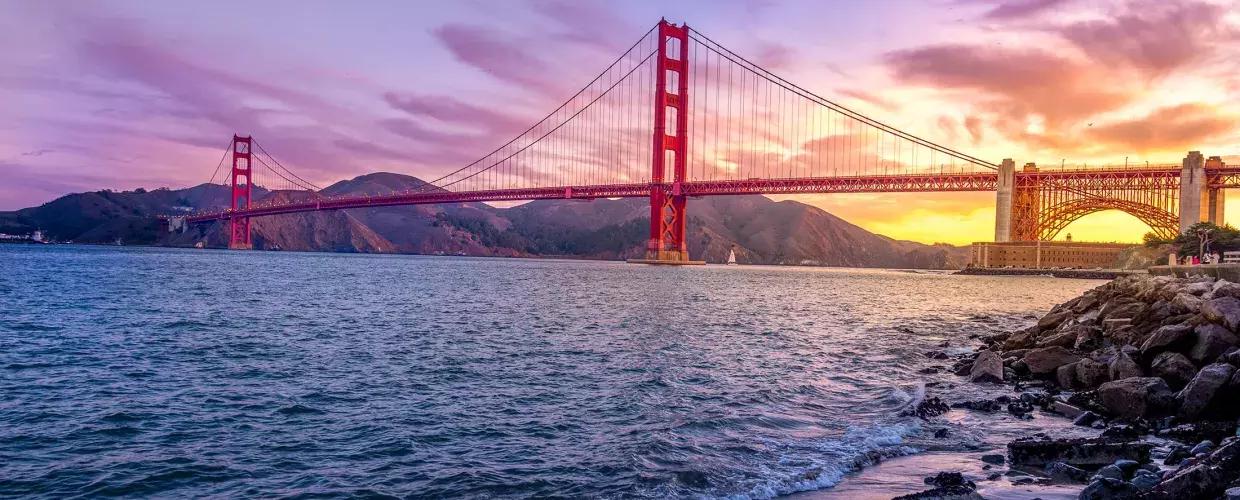 Il 金门大桥 al tramonto con un cielo multicolore e la Baia di San Francisco in primo piano.